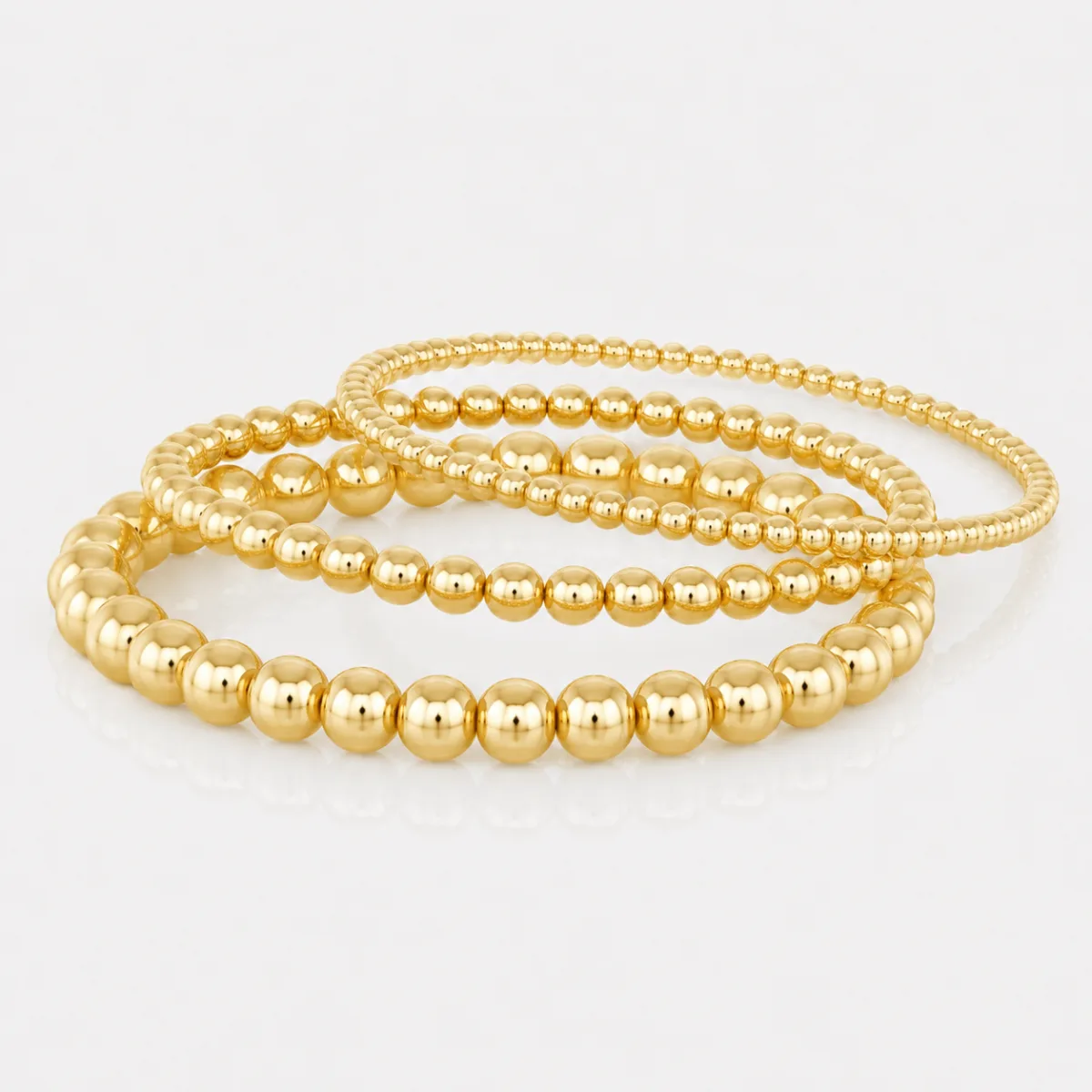 Best Stacking Bracelets Under $10: Read the Length Before You Buy 1 Three gold bead bracelets of increasing bead size resting together on a pale grey surface