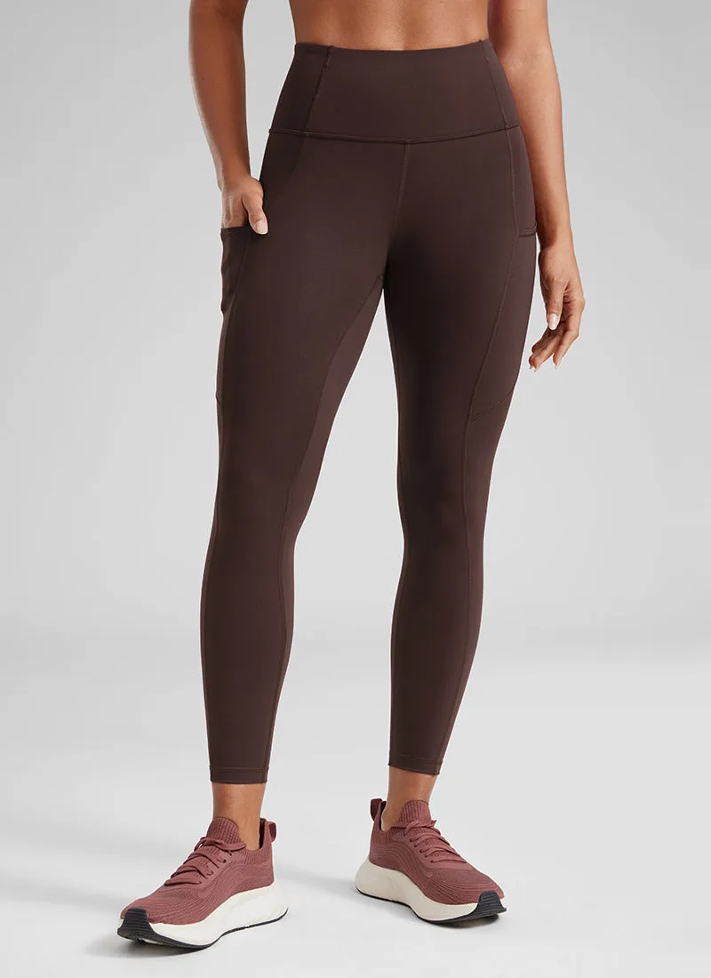 Espresso brown Nakedfeel legging with a hand tucked into the side thigh pocket, worn with rose coloured running shoes