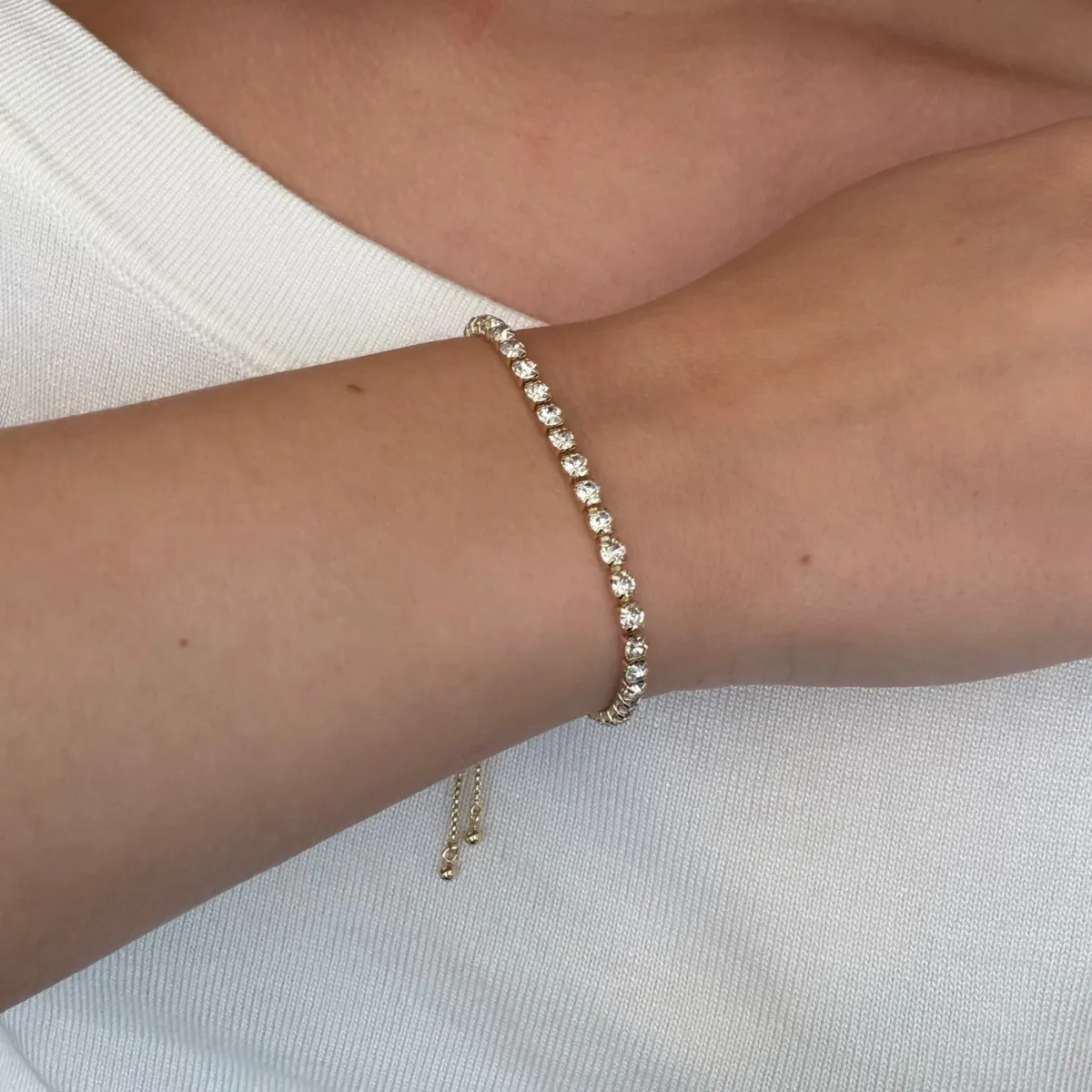 Best Stacking Bracelets Under $10: Read the Length Before You Buy 2 Thin gold tennis bracelet with a single row of clear stones fastened on a wrist, with the sliding clasp tail hanging below