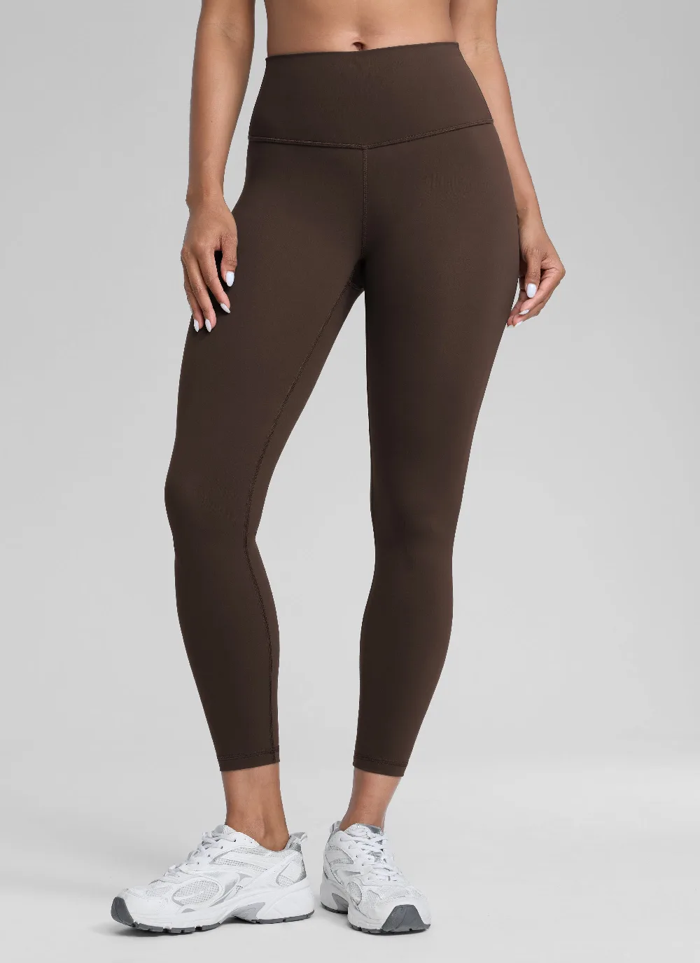 Dark brown high compression legging with a wide smooth waistband and no side pockets, shown front on with white sneakers