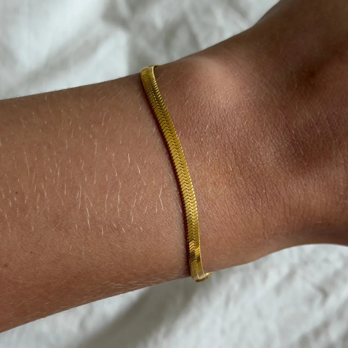 Best Stacking Bracelets Under $10: Read the Length Before You Buy 5 Flat gold herringbone chain bracelet worn snug on a wrist against a white fabric background