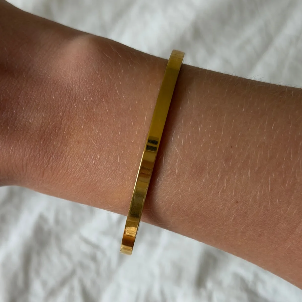 Best Stacking Bracelets Under $10: Read the Length Before You Buy 6 Slim flat gold bangle with an open gap at the underside of the wrist, worn against a white fabric background
