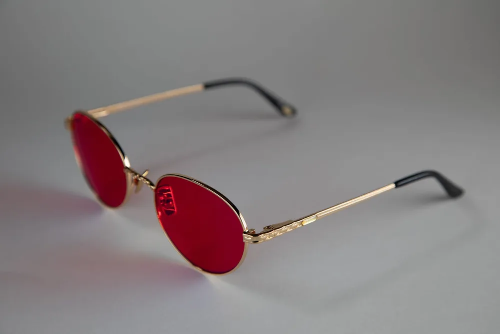 EMR-TEK Athena glasses on a grey backdrop, oval red lenses in a thin gold frame with black temple tips