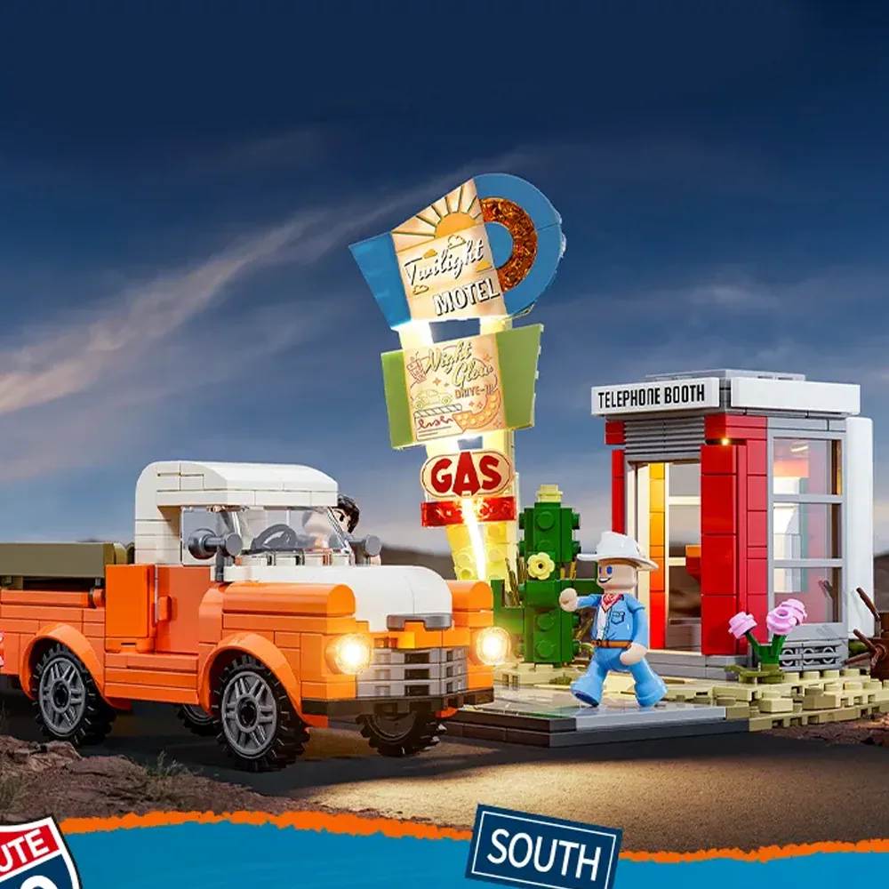 A lit roadside diorama with an orange pickup truck whose headlights are glowing, an illuminated motel and gas sign, and a red telephone booth lit from inside