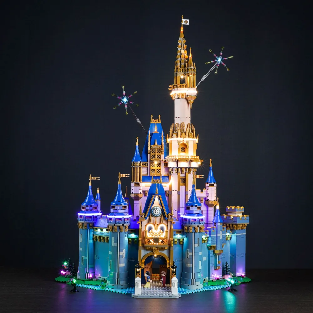 The LEGO Disney Castle lit at night, warm gold light in the towers and windows, blue and purple wash across the turrets and two firework light effects above the spires