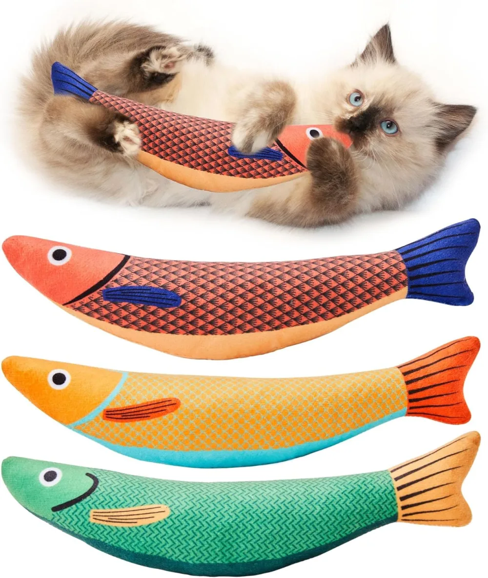 Three fabric fish shaped kicker toys in orange, yellow and green, with a fluffy cat above them holding the orange one between its paws