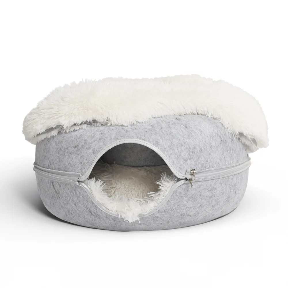 A grey felt donut shaped cat cave with a round tunnel opening and a zip running all the way around its circumference, a white fluffy plush mat inside and a matching plush cover draped over the top