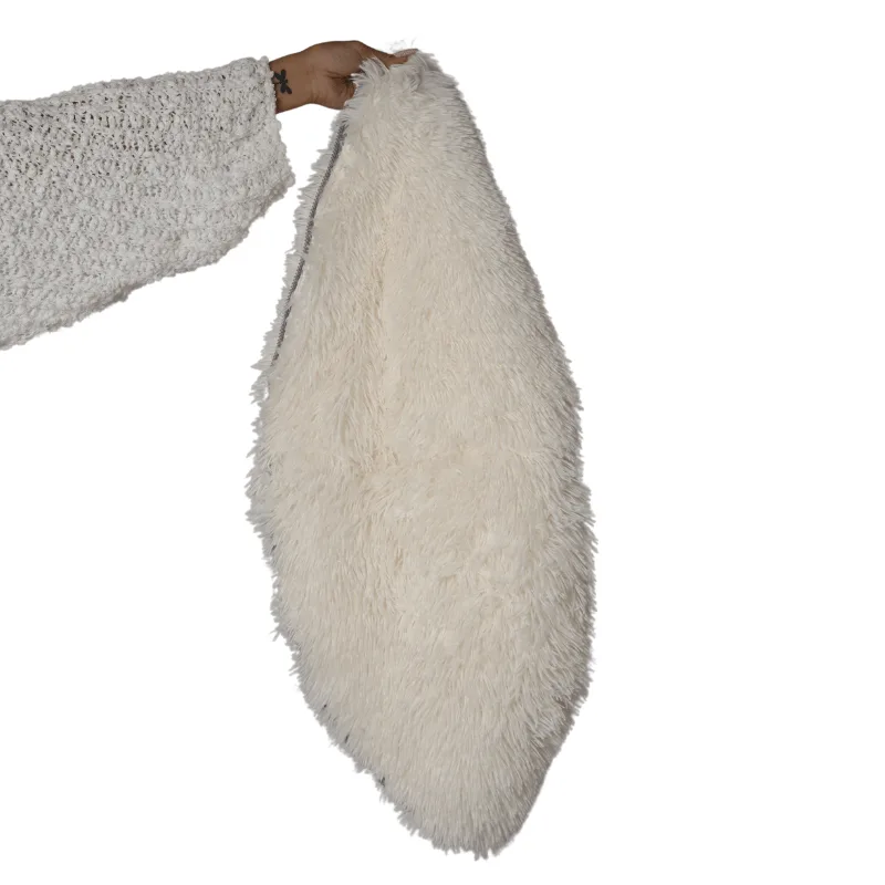 A hand holding up a cream coloured long pile plush cover for the cat cave, shown against a white background