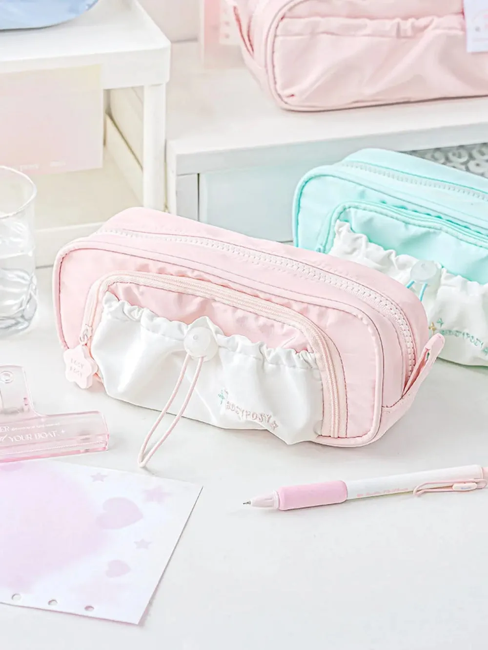 Best Journaling Supplies and Aesthetic Stationery: How to Build a Complete Kit in 2026 1 A pastel pink zipped pencil case with a white ruffled drawstring pocket on the front, shown beside a mint green version, with a pink gel pen and a sheet of hole-punched paper on a white desk