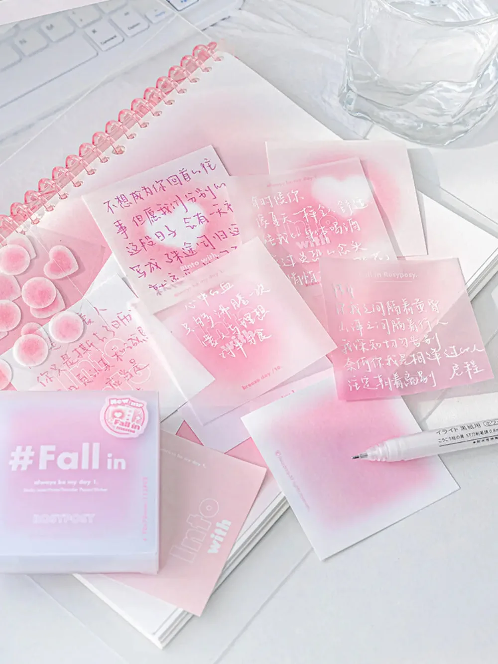Best Journaling Supplies and Aesthetic Stationery: How to Build a Complete Kit in 2026 7 A spread of pink gradient notepaper sheets with handwritten text, fanned out beside their frosted box labelled Fall in, on a white desk