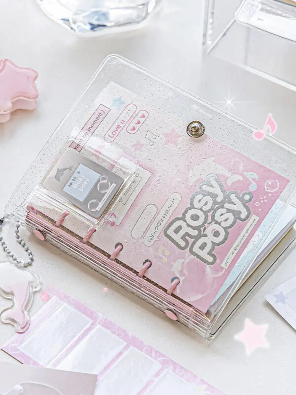 Best Journaling Supplies and Aesthetic Stationery: How to Build a Complete Kit in 2026 6 A pocket-sized M5 five-ring binder with a clear glitter PVC cover over a pink decorated insert, opened flat on a white desk beside sticker sheets