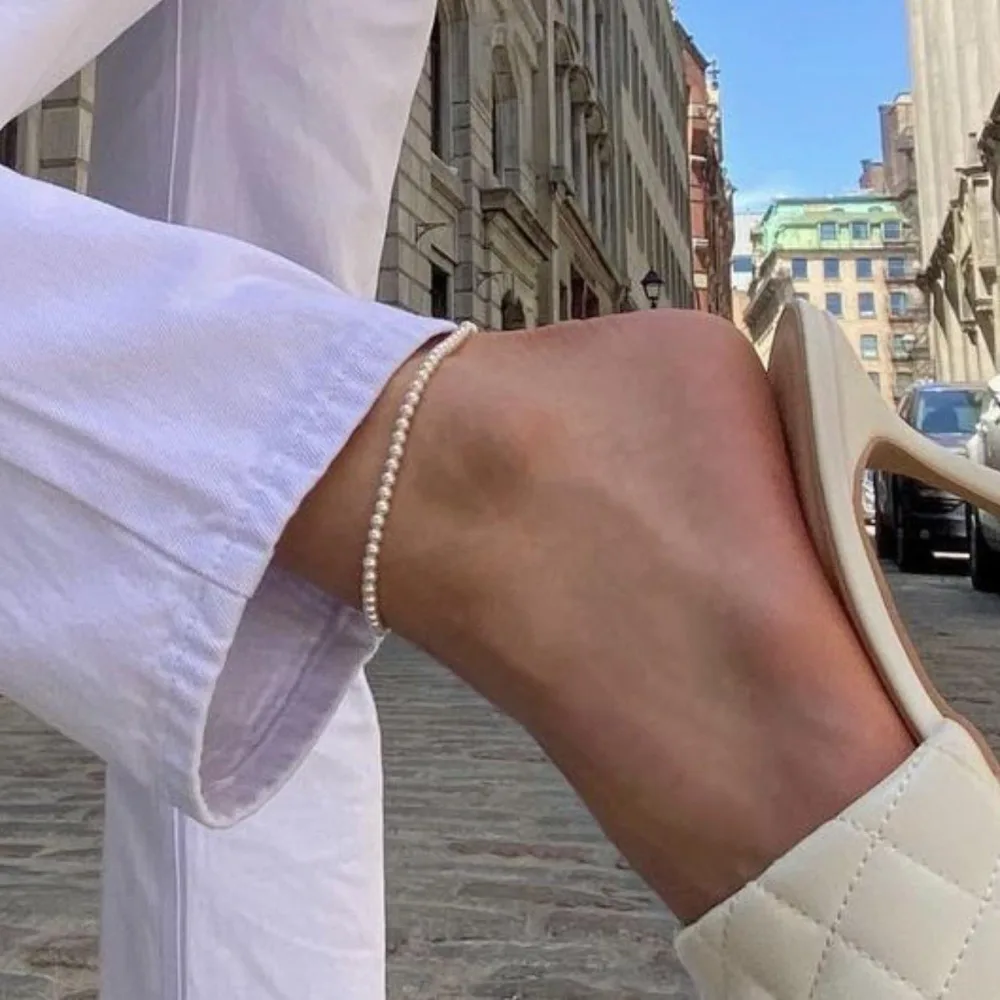 Best Waterproof Gold Jewelry Under $20: What Tarnish-Free Really Means 8 A slim anklet of small white pearls worn on an ankle above a cream loafer, photographed on a city street