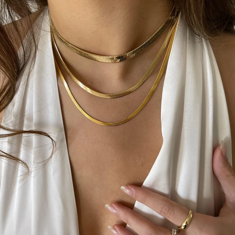 Best Waterproof Gold Jewelry Under $20: What Tarnish-Free Really Means 1 A woman wearing three flat gold herringbone snake chains at three different lengths over a white top, with a gold dome ring on one finger