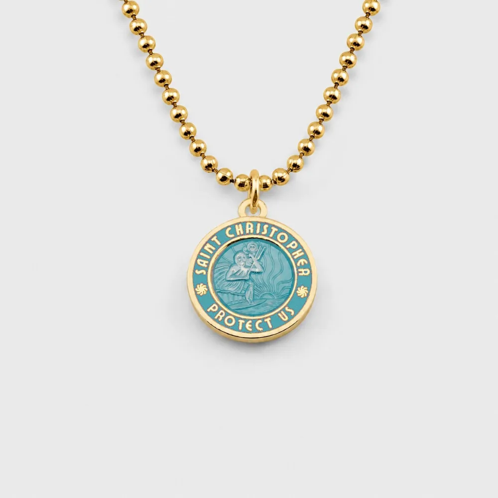 A gold St. Christopher medallion with teal enamel on a gold ball chain, the rim reading Saint Christopher Protect Us around a raised figure carrying a child across water