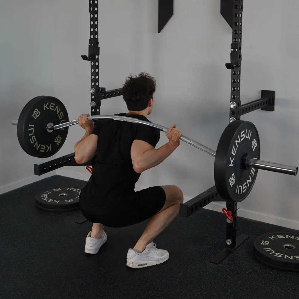 Best Specialty Barbells for Home Gyms: Trap, Swiss, Cambered and Buffalo Bars Compared 3 A man at the bottom of a back squat with the Beppu Buffalo Bar across his shoulders, the gentle forward curve of the shaft clearly visible