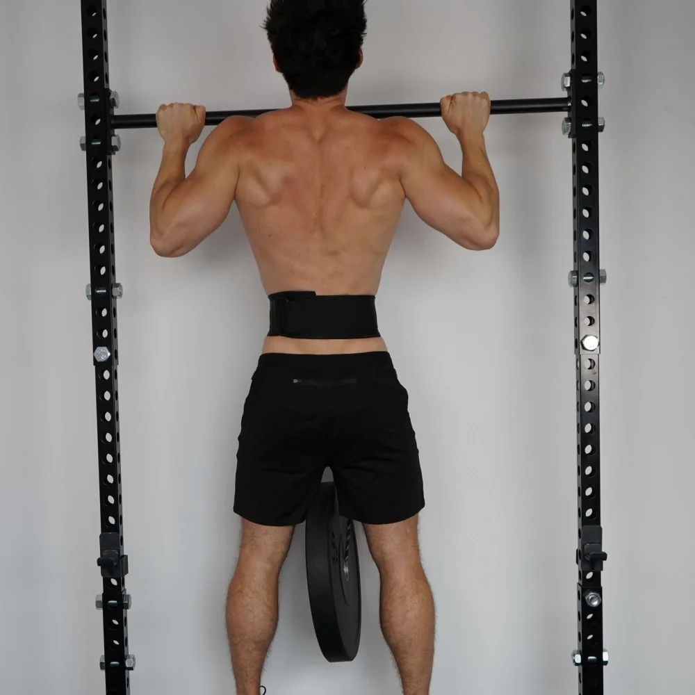 A man doing pull-ups on a rack mounted bar wearing the Duo-Belt around his waist with a bumper plate hanging behind him