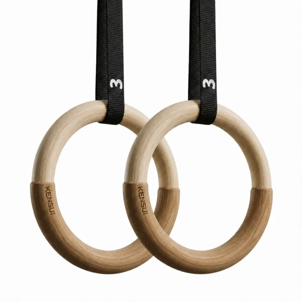 A pair of birch wood Kensui DUO-Rings hanging from numbered black nylon straps, the lower section of each ring visibly thicker than the upper section