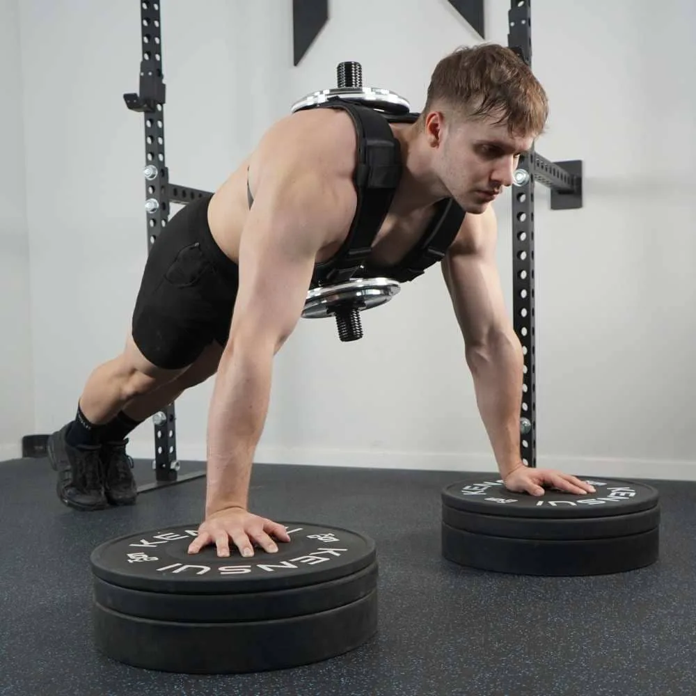 A man doing push-ups while wearing the loaded EZ-VEST, with both hands raised on stacks of bumper plates so the front loading post clears the floor