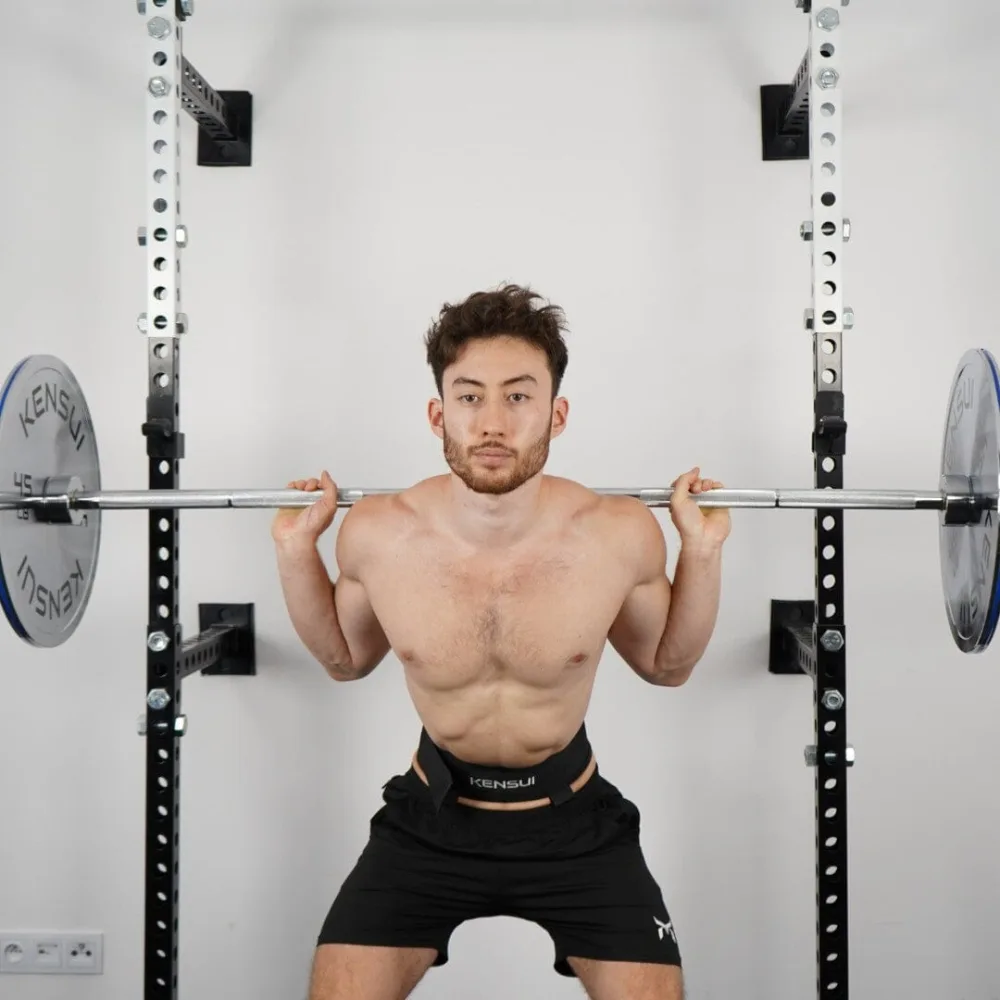 Best Specialty Barbells for Home Gyms: Trap, Swiss, Cambered and Buffalo Bars Compared 7 A man squatting in a rack with the Osaka Olympic Barbell, a plain straight chrome bar loaded with 45 pound plates