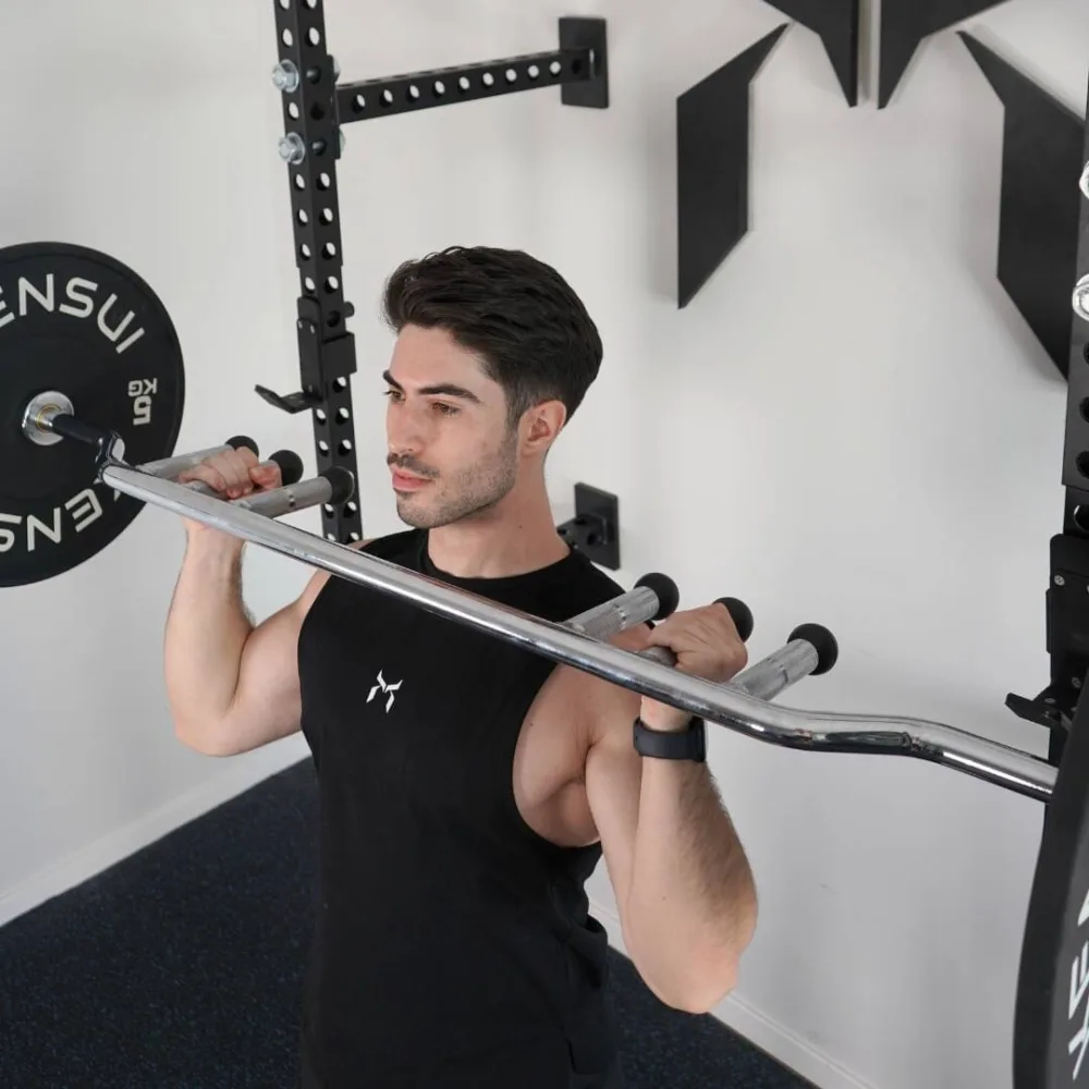 Best Specialty Barbells for Home Gyms: Trap, Swiss, Cambered and Buffalo Bars Compared 2 A man pressing the Sapporo Open Swiss Bar overhead in a rack, gripping two of the vertical neutral grip handles that hang below the shaft