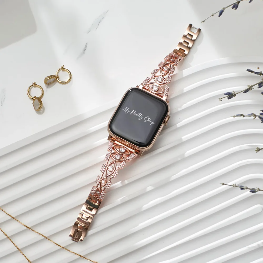 Best Apple Watch Bands That Look Like Jewelry 4 A rose gold Apple Watch on a strap of crystal set marquise shaped links, laid flat beside gold hoop earrings and sprigs of lavender